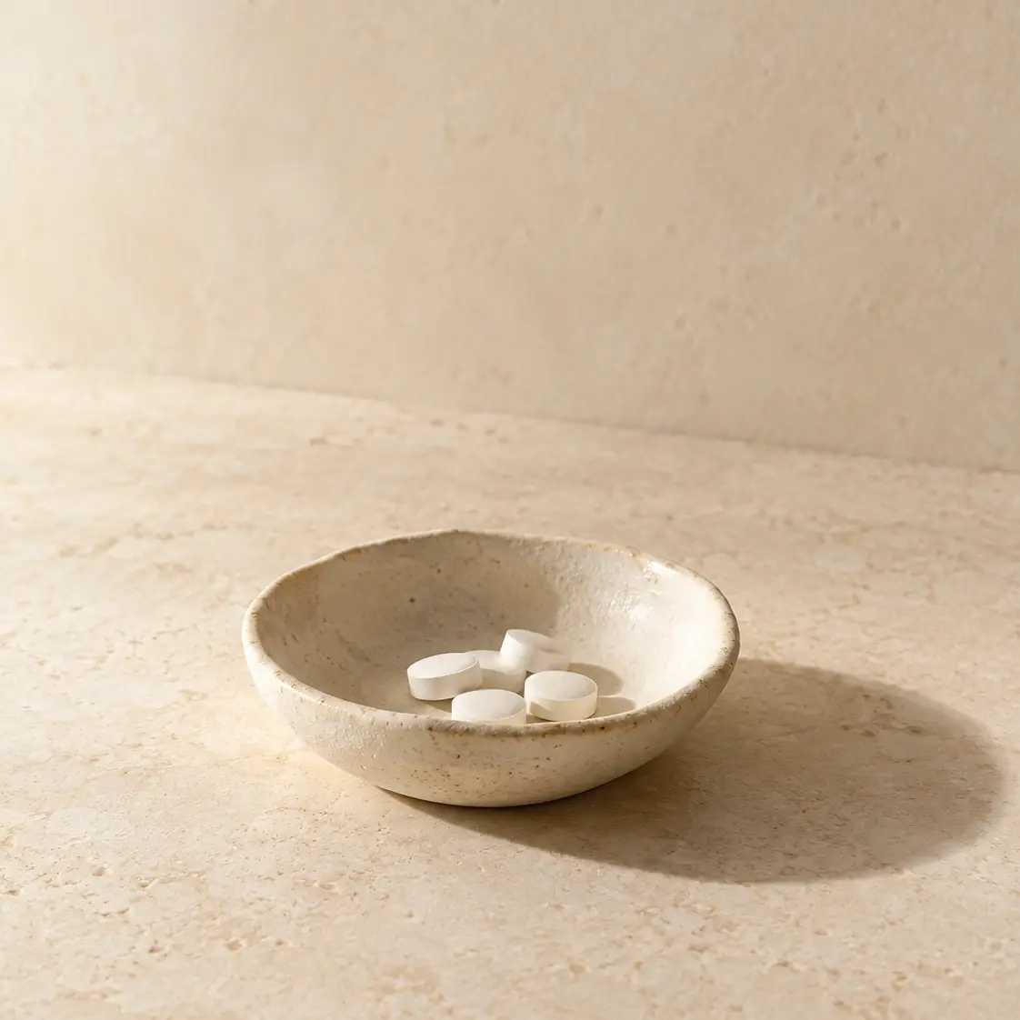 White tablets in a small ceramic dish on warm limestone